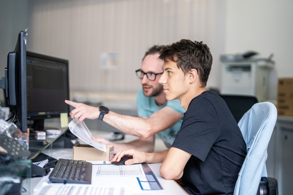Ausbilder erklärt einem Lehrling eine Aufgabe am Computer