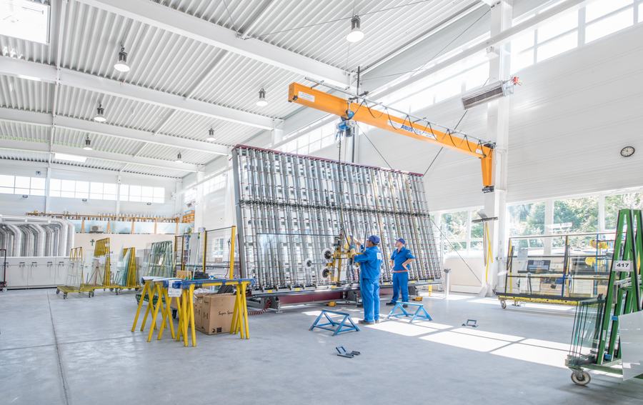 Mitarbeiter heben mit Kran und Vakuumheber eine große Glasscheibe in der Werkstatt