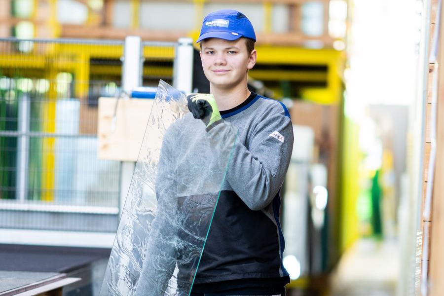 Lehrling Glasbautechnik hält eine Glasscheibe in der Werkhalle