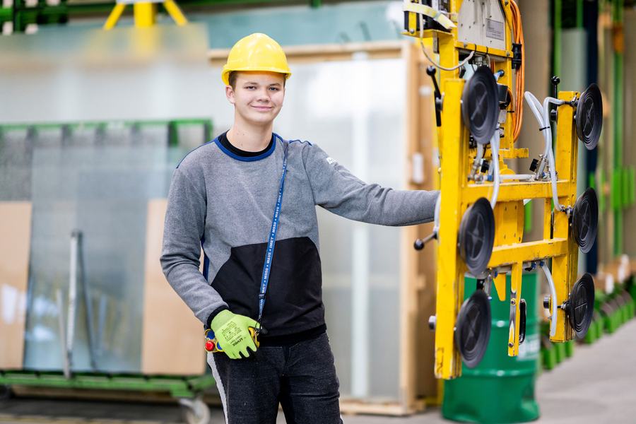 Lehrling Glasverfahrenstechnik mit Schutzhelm neben einem Vakuumheber für Glasscheiben