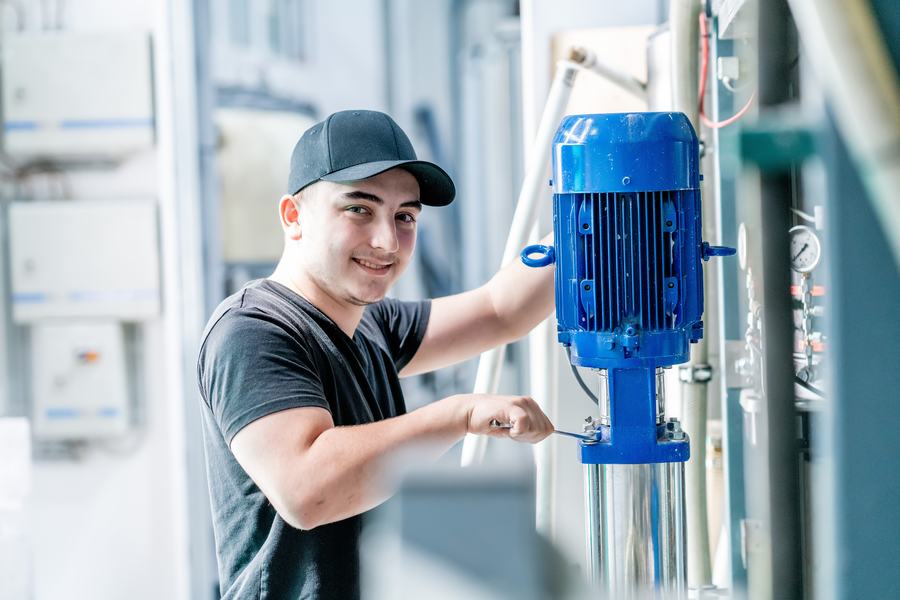Lehrling Prozesstechnik arbeitet mit einem Schraubenschlüssel an einer Pumpe einer Produktionsanlage